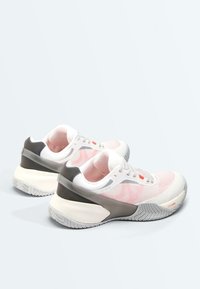 Paire de baskets blanches et roses avec des semelles épaisses beige et grises, positionnées dans des directions opposées.