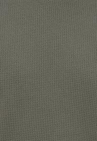 Υφή υφάσματος με γκρι πλέξη βάφλας, με μικρά, ομοιόμορφα ανυψωμένα τετράγωνα μοτίβα που καλύπτουν ομοιόμορφα την επιφάνεια.