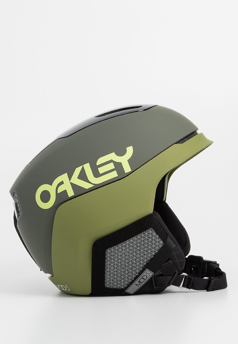 Casco de esquí verde y negro con un exterior liso, prominente logo de "Oakley" en amarillo, ventilación lateral de malla y correa de mentón ajustable.