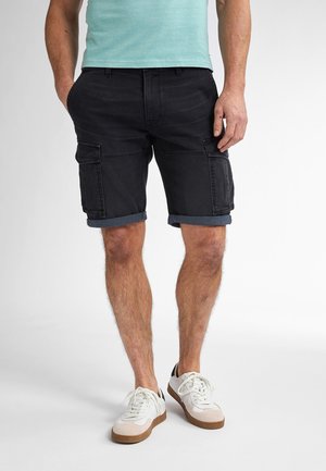 Sorte cargo shorts med op rullede kanter, der har sidelommer og denimtekstur. Båret med hvide sneakers og en lys blå skjorte.