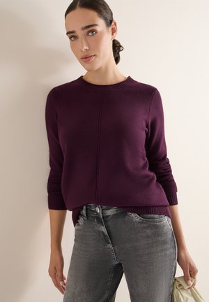 Lila gestrickter Pullover mit rundem Ausschnitt und gerippten Bündchen, kombiniert mit grauen Jeans. Vorteilhafte Textur; minimalistische Gestaltung.