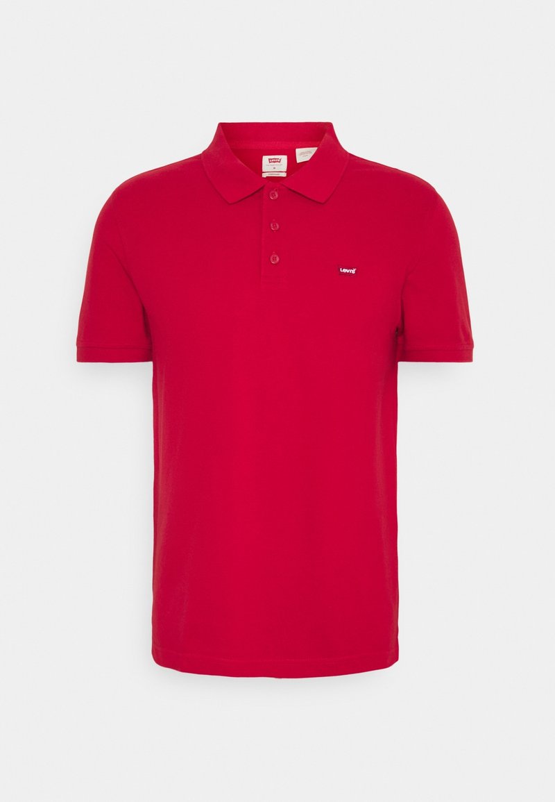 Polo rouge en coton, avec un col classique, trois boutons, et un petit logo sur la poitrine gauche. Texture lisse et manches courtes.