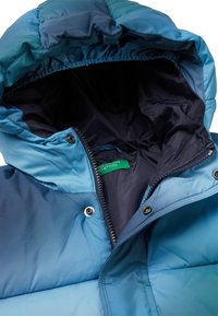 Chaqueta ligera y acolchada en tonos degradados de azul, con capucha, cierre de cremallera, forro interior y etiqueta de logo. Textura sintética suave.