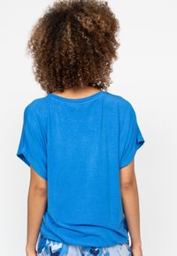 Koninklijk blauwe T-shirt, korte mouwen, losse pasvorm, zachte stof, ronde hals, gedetailleerde textuur, gedragen met gemusterde blauwe broek.