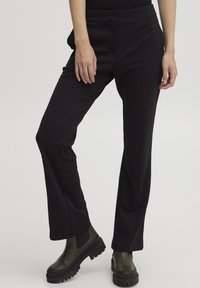 Zwarte op maat gemaakte broek met een recht model, voorzien van een soepele textuur en zijzakken, gecombineerd met stevige groene enkelbotten.