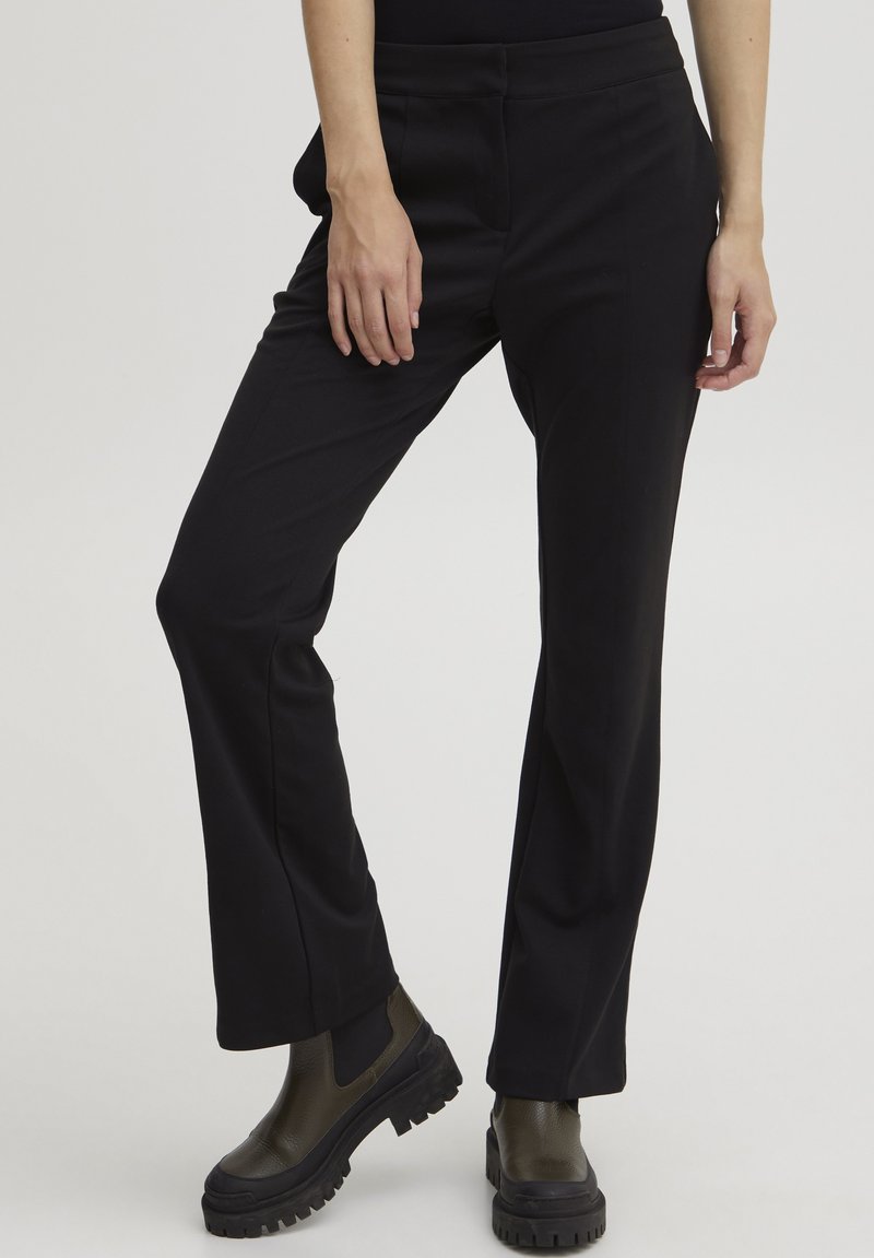 Zwarte op maat gemaakte broek met een recht model, voorzien van een soepele textuur en zijzakken, gecombineerd met stevige groene enkelbotten.