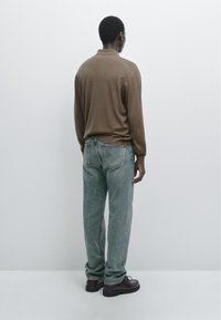Brown long-sleeve pullover, loose-fit, paired with light blue straight-leg jeans. Dark shoes complete the casual look from a back view.