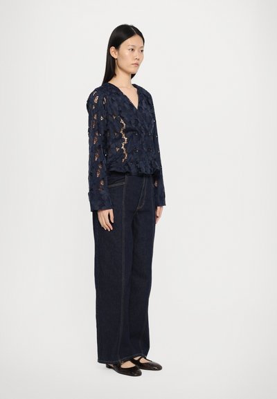 Navy blue lace blouse with floral cutouts, paired with high-waisted dark denim jeans featuring subtle stitching and wide legs.