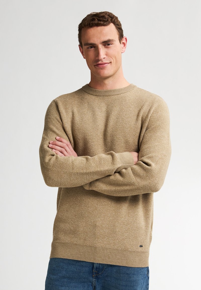 Beige gebreide trui met ronde hals, lange mouwen, geribbelde manchetten en zoom, met een textuurstof en een klein logo aan de onderzijde.