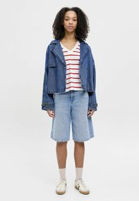 Chaqueta de mezclilla con grandes solapas, una camiseta de cuello en V blanca y roja a rayas, pantalones cortos de mezclilla azul claros y zapatillas beiges con acentos oscuros.