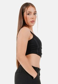 Top corto nero a costine con un design aderente, abbinato a pantaloni a vita alta. Il top presenta un scollo a barca e dettagli strutturati.
