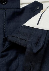 Navy fabric with a textured finish, featuring a white accent, zip pocket, and button detail. Stitching is clean and reinforced.