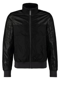 Veste noire zippée avec col montant, poignets et ourlet côtelés, présentant un panneau supérieur lisse et des manches longues matelassées.