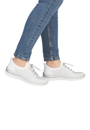 Person wearing blue jeans and white knit sneakers with laces, shown from mid-calf down against a white background.