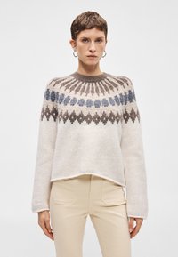 Πλεκτό πουλόβερ σε κρεμ απόχρωση με στρογγυλή λαιμόκοψη. Διαθέτει περίπλοκα γεωμετρικά σχέδια σε μπλε και καφέ. Μακριά μανίκια και χαλαρή εφαρμογή.