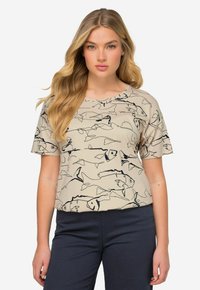Top corto de manga corta en color beige con un patrón de peces negros. Está hecho de una tela suave, tiene un escote redondo y un corte holgado, ideal para un look casual.