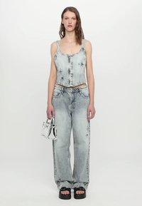 Light blue denim crop top with front buttons, paired with wide-leg jeans featuring distressed details. Accessories include a metallic handbag.