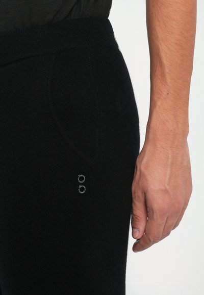 Fekete kötött jogger nadrág, textúrált felülettel, két kör alakú fém díszítéssel az oldalon és puha derékrésszel.