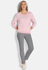 Hellrosa gestreifter Pullover mit Dreiviertelärmeln, kombiniert mit grauen Slim-Fit-Hosen und weißen Sneakern, vor einem schlichten Hintergrund stehend.