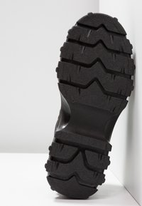 Semelle en caoutchouc noir avec des crampons profonds en zigzag et rectangulaires, conçue pour l’adhérence et la durabilité des chaussures.