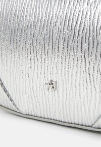 Srebrna teksturowana torba z pionowymi liniami, z subtelnym akcentem w postaci logo. Materiał wydaje się syntetyczny o połyskliwym wykończeniu.