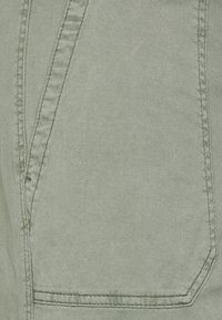 Tissu vert clair à texture lisse, présentant des coutures visibles et un détail de poche le long du bord.