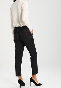 Svarta, tapered byxor med en strukturerad tyg och elastisk midja, i kombination med en ljusbeige långärmad topp och svarta högklackade skor.