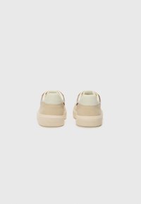 Beige sneakers with a smooth upper, a textured heel, and a chunky cream-colored sole. Features a minimalist design with no patterns.