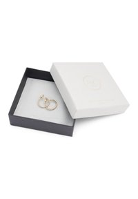 Pendientes de aro dorados exhibidos en una caja negra con un interior gris y una tapa blanca texturizada que presenta un logotipo en relieve.