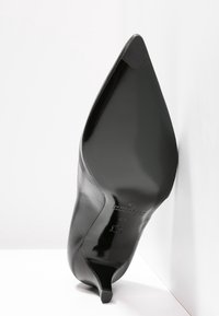 Musta nahkasaapas korkealla korolla, jossa on terävä kärki ja kiiltävä pinta, varustettu hoikalla stiletto-korolla ja minimalistisilla muotoiluainoilla.