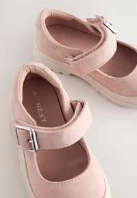 Zapatos Mary Jane de ante rosa con una correa y hebilla plateada, con punta redonda y suela de goma blanca con textura.