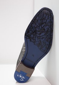 Semelle de chaussure de couleur bleu marine avec un motif de chaussures répété et une surface texturée grise au niveau du talon. Taille 7½ estampillée sur la semelle.