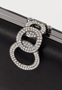 Μαύρη σατέν clutch με μεταλλικό κλείσιμο που διαθέτει τρία συνδεδεμένα κύκλους διακοσμημένα με διαυγή ρινοστάτες, προσφέροντας μια λαμπερή πινελιά.