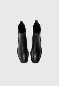 Bottines en cuir noir avec un bout pointu, texture lisse, panneaux latéraux élastiques et languettes pour un enfilage facile.