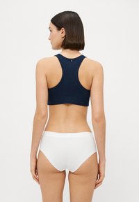 Mørkeblå sportshåndkle med racerback-design, glatt tekstur og et lite emblem bak. Kombinert med hvite mid-rise truser.