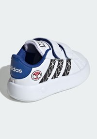 Vit sneakers med svart nätmönster, blå hälaccent och dubbla kardborreband. Har en röd och svart Spider-Man-logotyp på sidan.