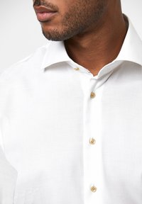 Witte button-up shirt met een eenvoudige geweven textuur, met een klassieke kraag en beige knopen langs de voorkant.
