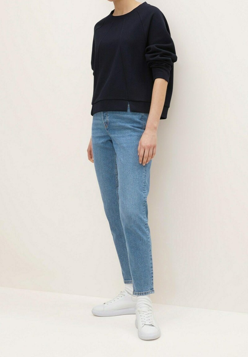 Marinblå texturerad sweatshirt med rund hals, kombinerad med ljusblå raka jeans och vita sneakers. Enkel och avslappnad outfit.