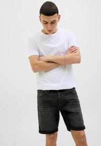 Tricou alb cu mânecă scurtă, asortat cu pantaloni scurți din denim negri, cu tiv răsucit. Materialul are o textură fină și o decolorare subtilă.