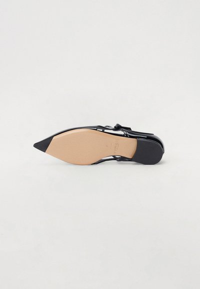Chaussure noire à bout pointu avec une finition brillante, dotée d'une fine bride et d'une semelle beige. Le talon est bas et légèrement plus large à l'arrière.
