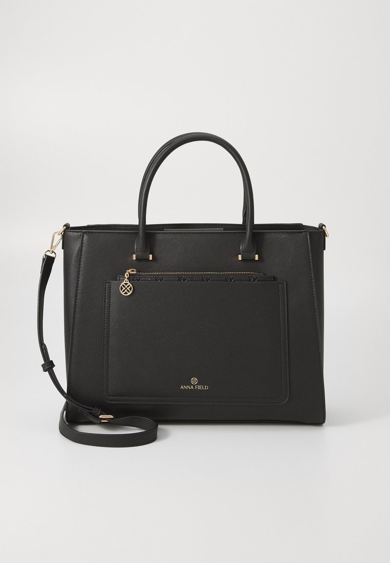 Black synthetic handbag with structured shape, dual top handles, detachable shoulder strap, front zip pocket, and gold logo accent.