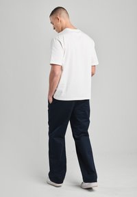 T-shirt en coton blanc avec une coupe classique, associé à un pantalon bleu marine, avec une jambe droite et des poches. Modèle de dos.