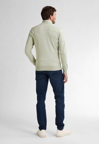 Pulover verde deschis cu guler înalt, design ajustat și detalii cusute. Asortat cu blugi negri și adidași bej.