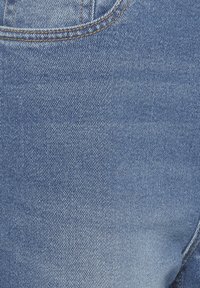 Gros plan sur un tissu en denim bleu clair avec des coutures visibles et une couture de poche, montrant les détails de la texture et du tissage.