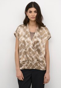 Top avvolgente marrone con motivo, maniche corte, texture liscia e scollatura a V, abbinato a una maglietta beige e pantaloni scuri.