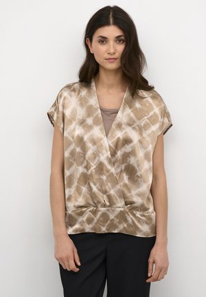 Top envolvente marrón con estampado, de mangas cortas, textura suave y escote en V, combinado con una camiseta interior beige y pantalones oscuros.