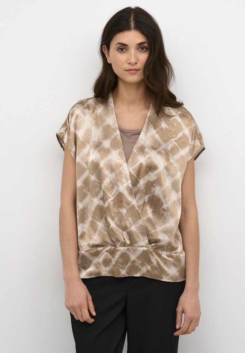 Top avvolgente marrone con motivo, maniche corte, texture liscia e scollatura a V, abbinato a una maglietta beige e pantaloni scuri.