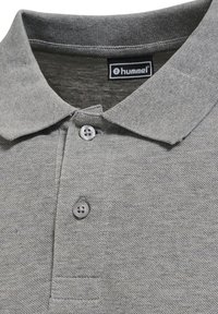 Polo gris con tejido texturizado, dos botones y cuello. La etiqueta de la marca es visible en la zona del cuello.