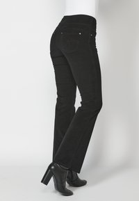 Pantalones vaqueros de mezclilla negra con un ajuste slim, que cuentan con una cintura de altura media, cuatro bolsillos y costura en el bolsillo trasero. Combinados con botines negros de tacón.