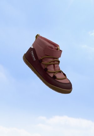 Botte d’enfant Viking rose et marron avec lacets jaunes et bride velcro sur fond de ciel bleu.